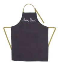 Load image into Gallery viewer, The soft, grey sand washed cotton linen of the Annie Sloan Apron, with contrasting green tie backs, makes for both comfortable and practical wear. The large double front pocket is the ideal place to store tin openers, mixing sticks and brushes, and the adjustable neck length means it will suit any height of painter. With the iconic Annie Sloan signature emblazoned in silver.